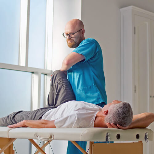Мужчина врач, чтото делает с коленом мужчины пациента лежащего на кушетке